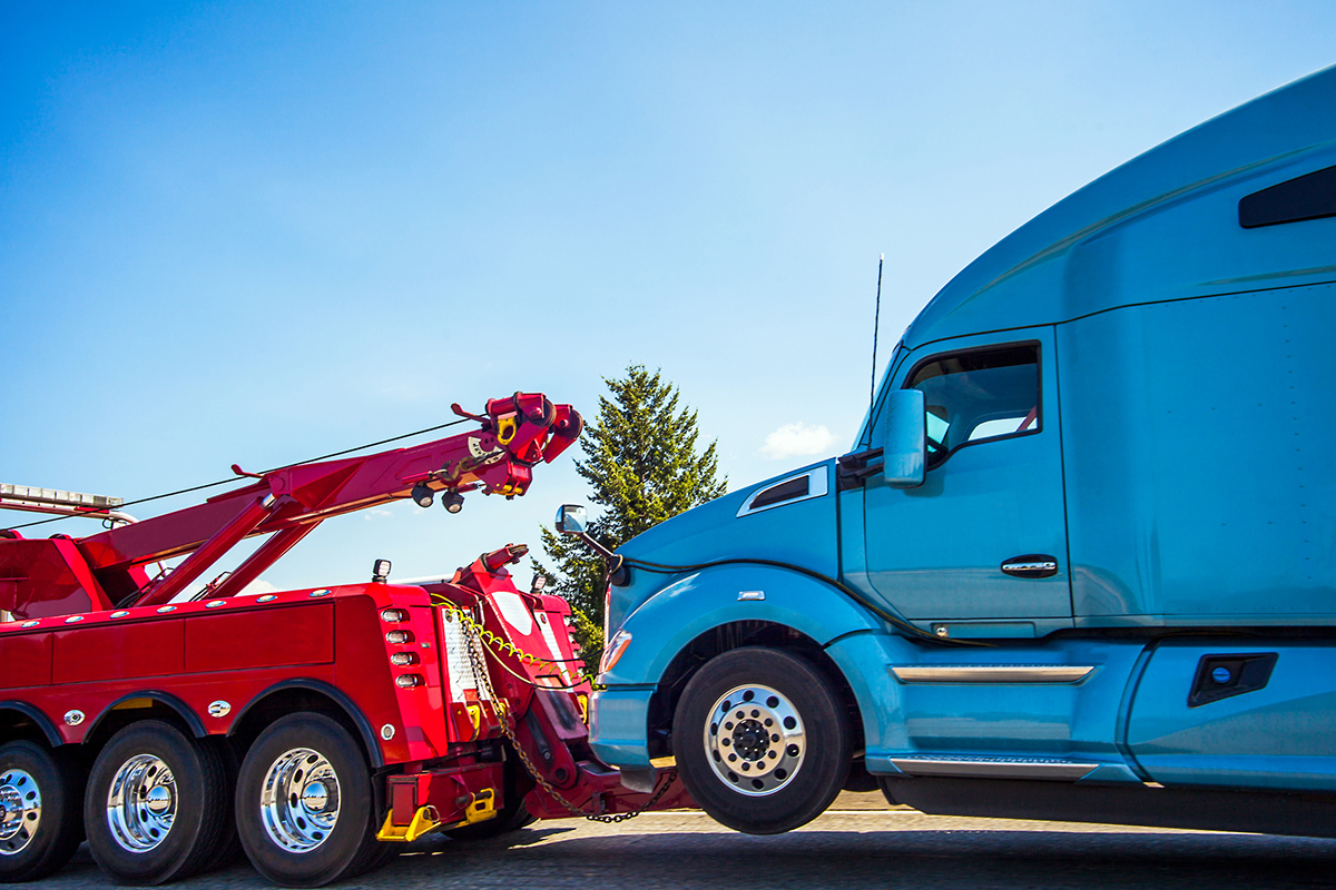 a red tow truck hauling a blue semi truck