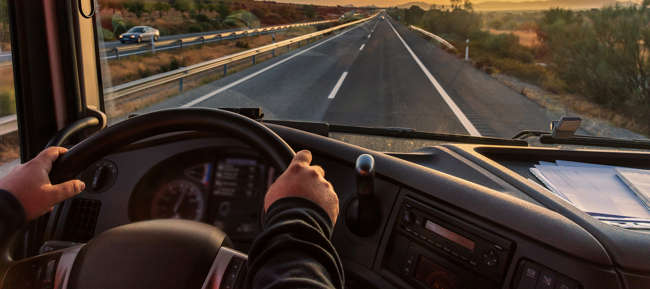 Inside view of a truck cab on a divided highway where we see a driver safety program driver safely navigating the road.